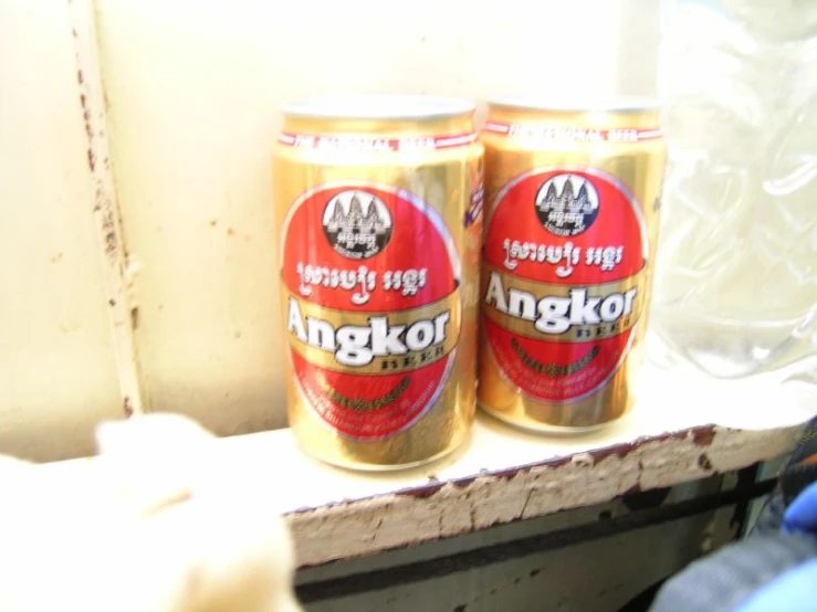 two cans of angcko, both orange and red, sitting on a window sill