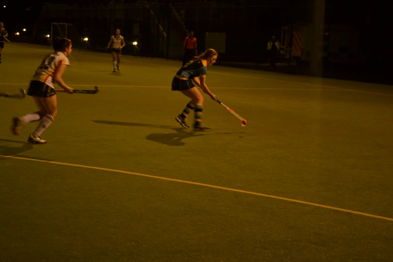 two girls playing hockey on an ice rink at night