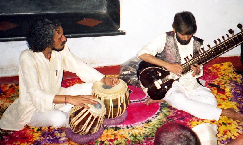 two people sit on a floral carpet playing musical instruments