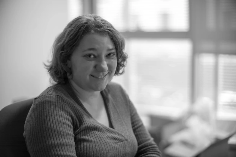 a black and white image of a smiling woman sitting in her office