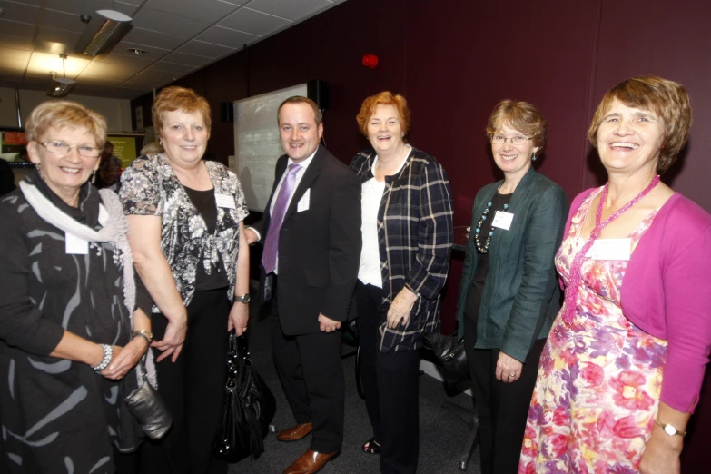 five women and a man in suits smiling for a po