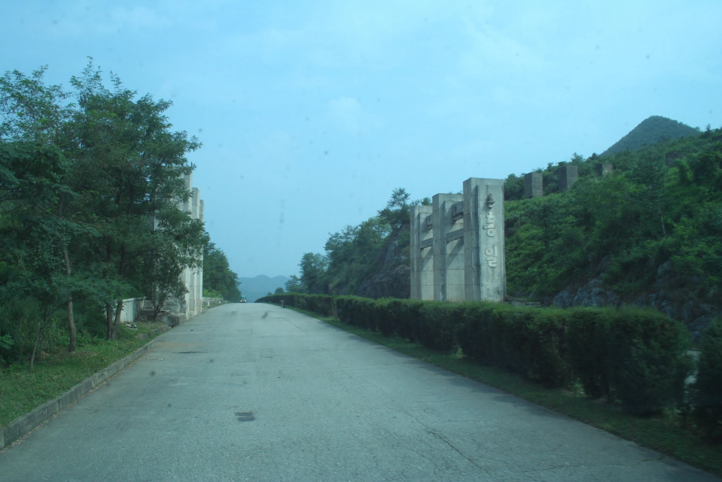 a road surrounded by hedges and trees near a mountain