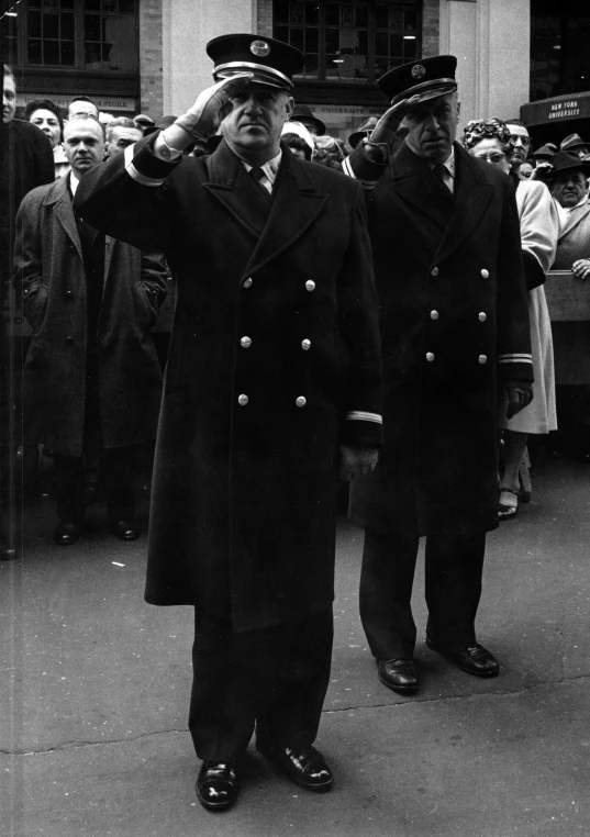 two men in naval uniforms saluting to the crowd