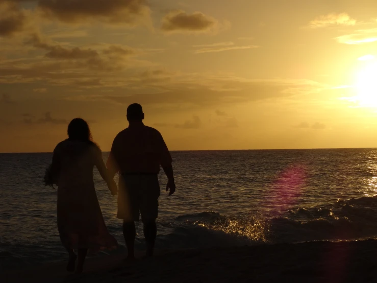 a couple walking towards the ocean at sunset