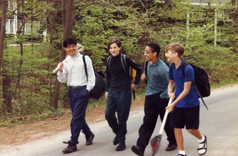 four boys walking down a road while holding baseball bats