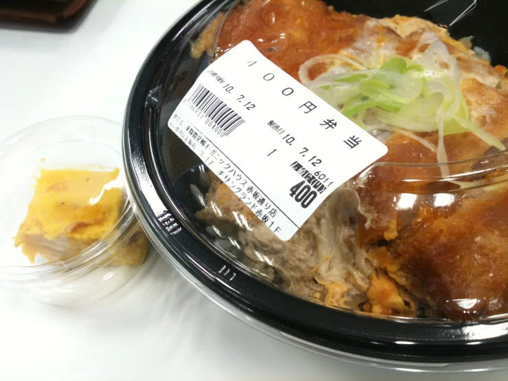 a container of food with a menu on it and a plastic lid with a fork stuck in it