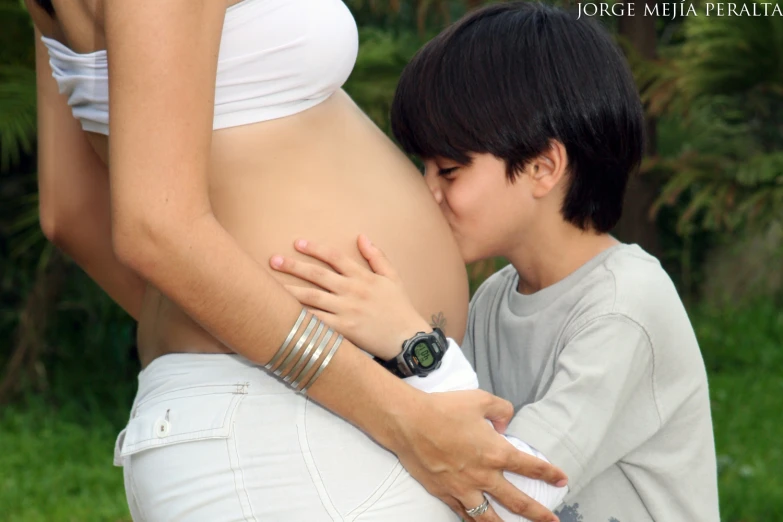 a boy kissing the belly of his pregnant mother