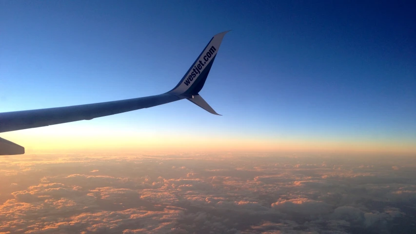 a airplane wing with the sun peeking through the clouds