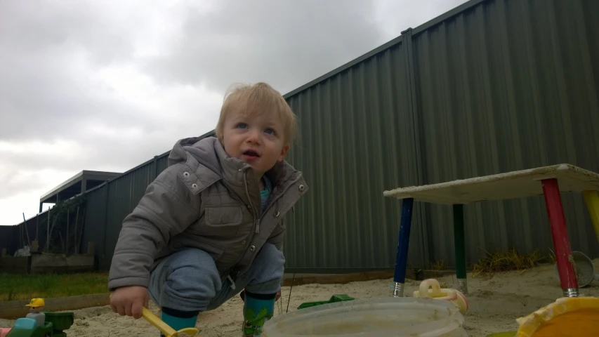 a baby with a coat and boots standing by a play area