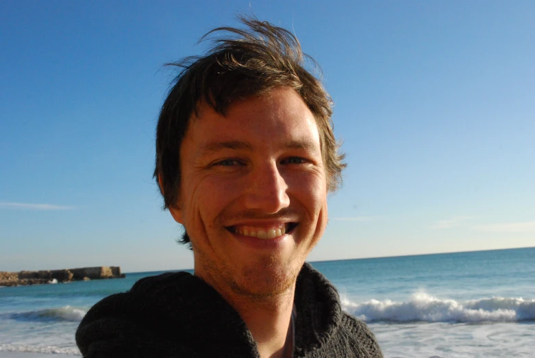 a man smiling while standing on the beach