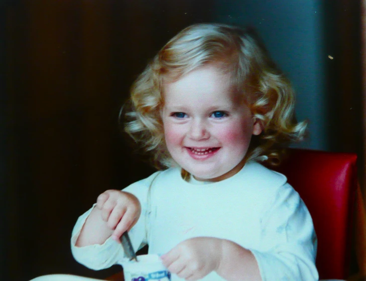 a child smiling as she eats her plate with chop sticks
