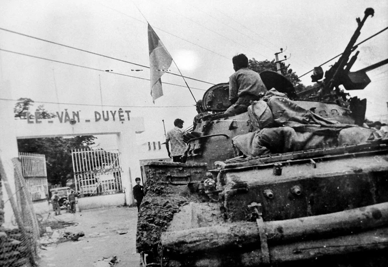 two men riding on top of an army tank