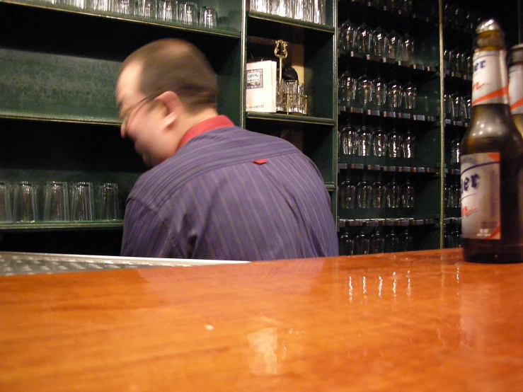 the man looks behind as he is sitting in front of a large bottle of alcohol