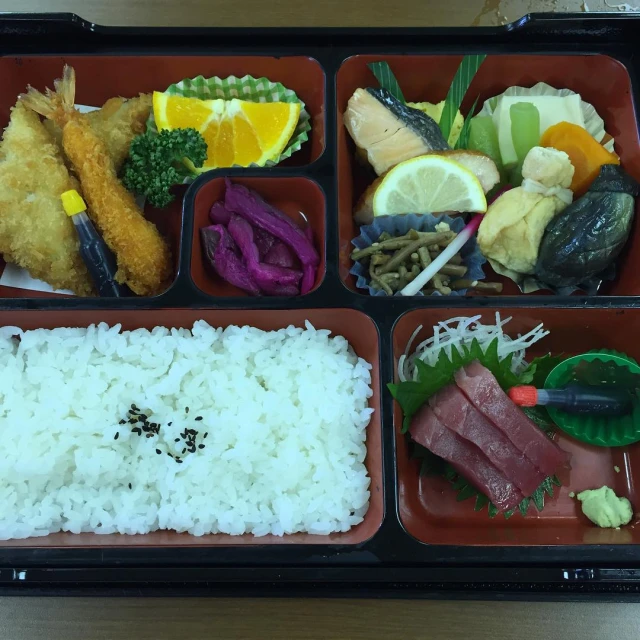 a bento box of food containing rice, vegetables and fish