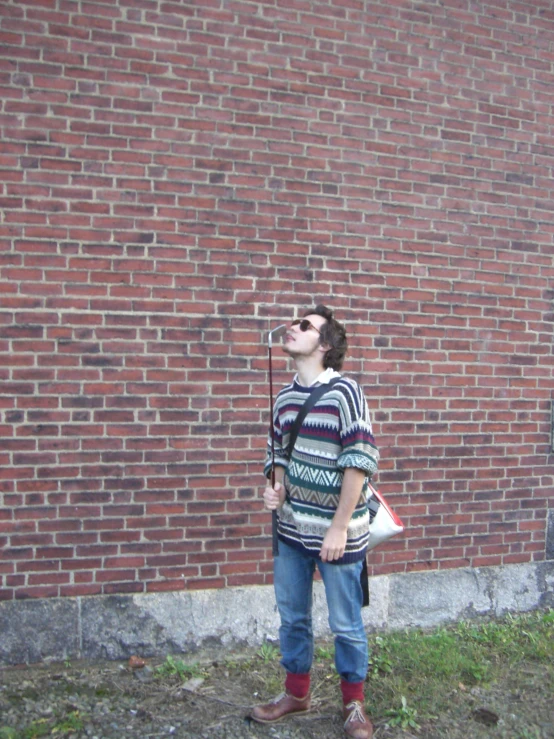 a man standing in front of a red brick wall holding a baseball bat