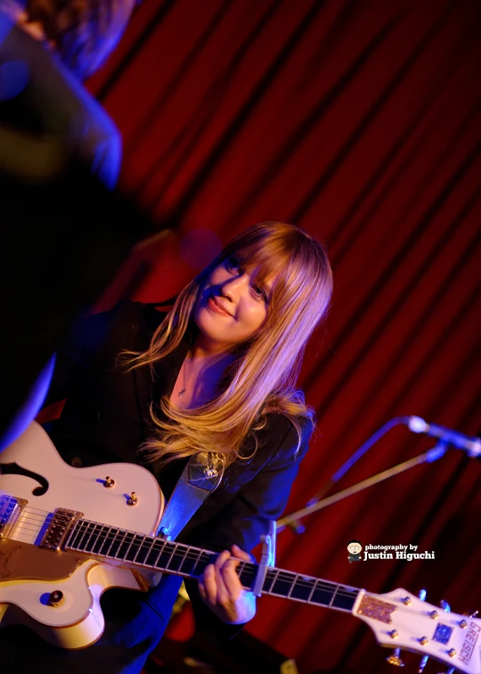 woman smiling with guitar in foreground and singing into a microphone