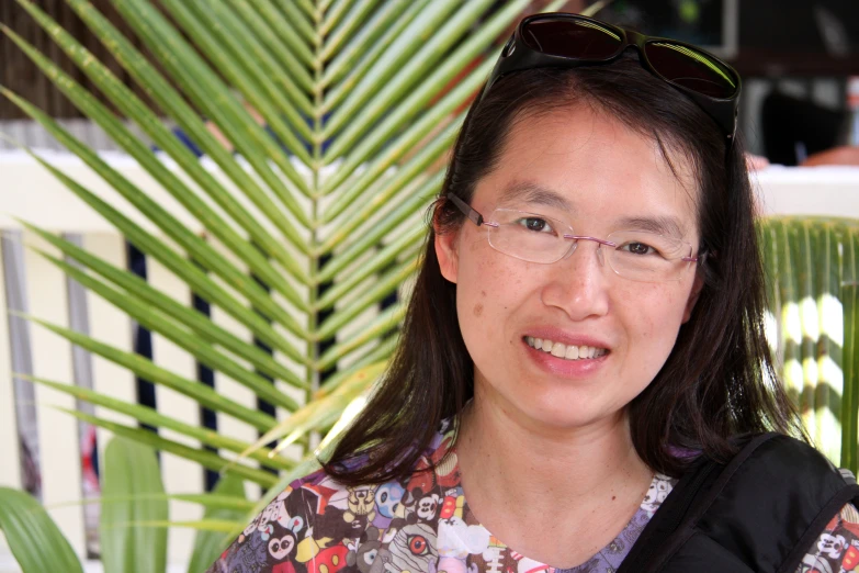 a woman with glasses standing near palm leaves