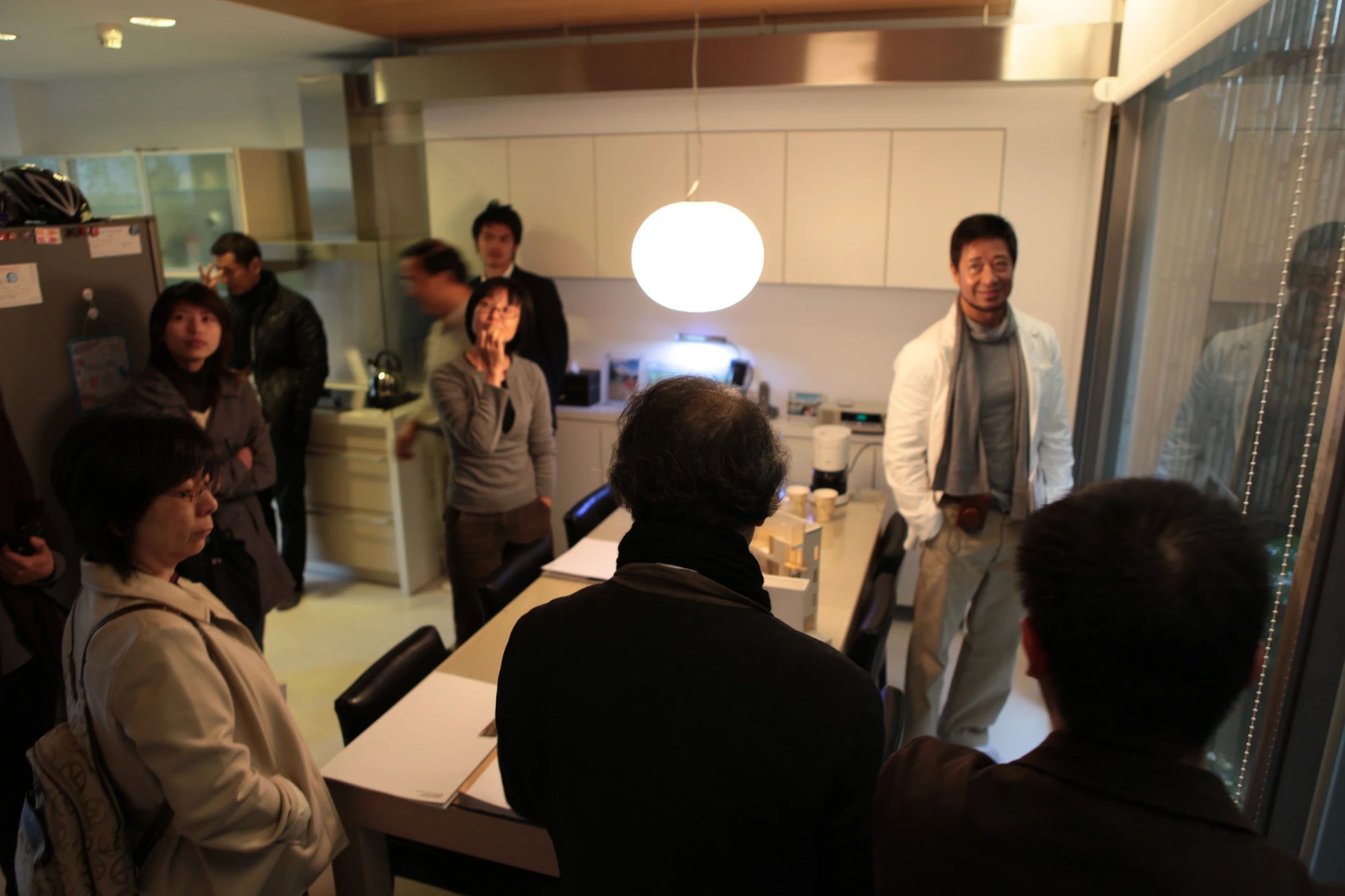 people are standing around in the kitchen, several standing around looking at soing