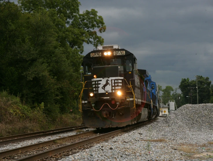 a train engine carrying carts down a track next to trees