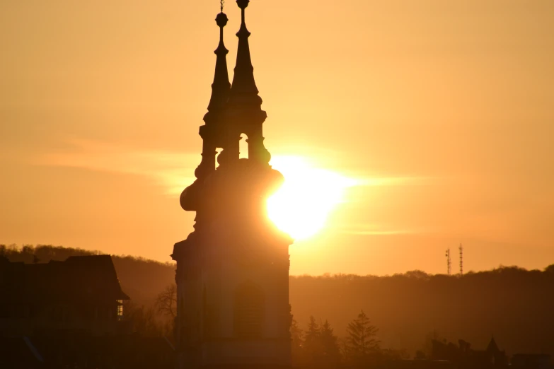 the sun is setting over a tower with steeple tops