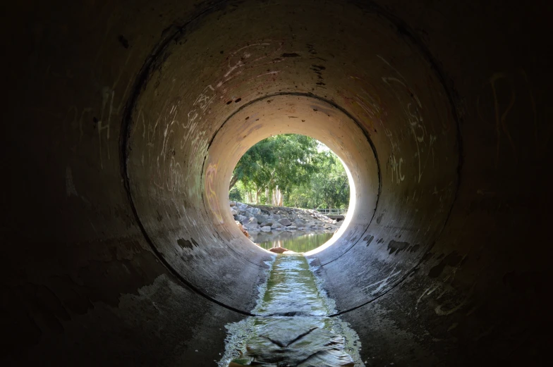 a drain running through a tunnel with trees in the background