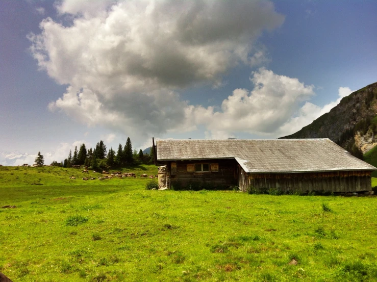 an old cabin is surrounded by mountains and grass