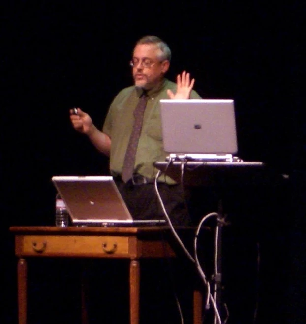 a man in a tie speaking to students on their laptops