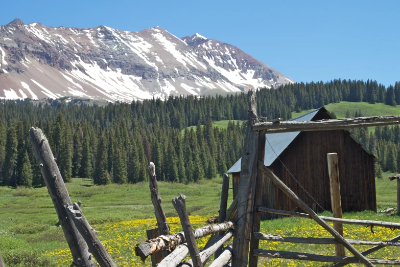 a wooden fence with a barn in the distance near snow - capped mountains