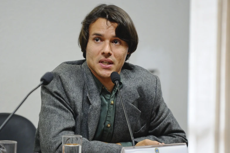 a young man in suit sitting at a table with microphone