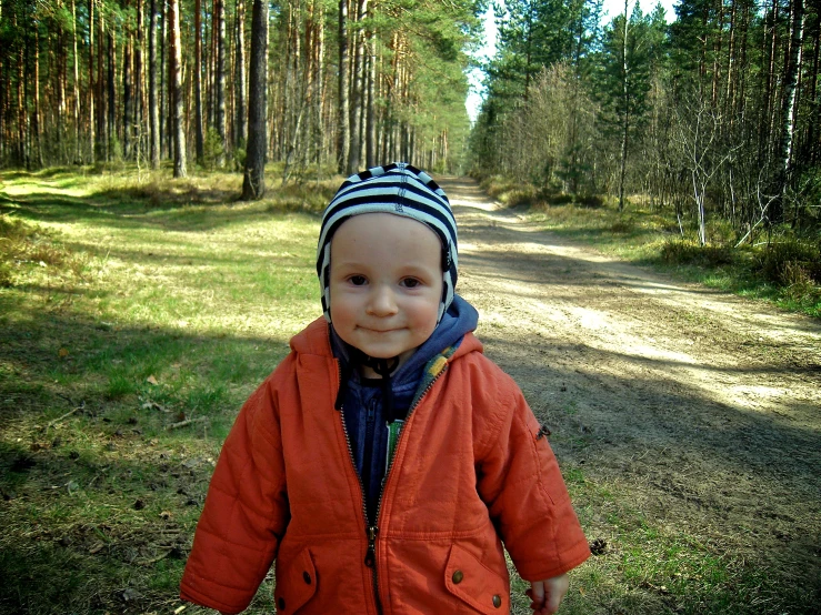 a little boy is standing in the dirt near the woods