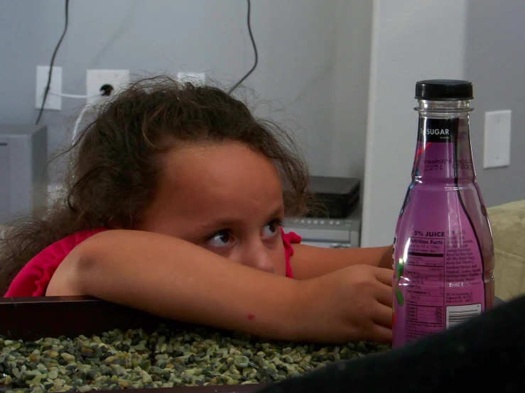 little girl laying in front of a bottle of g juice