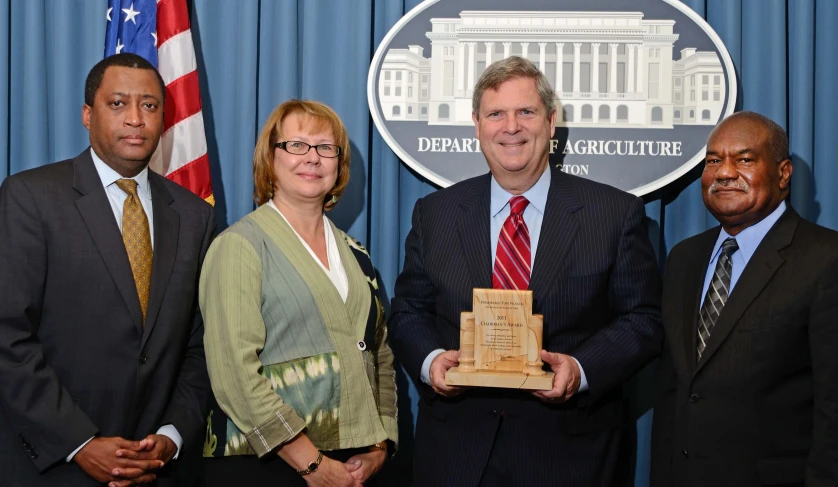 three business people with an award standing in front of a flag