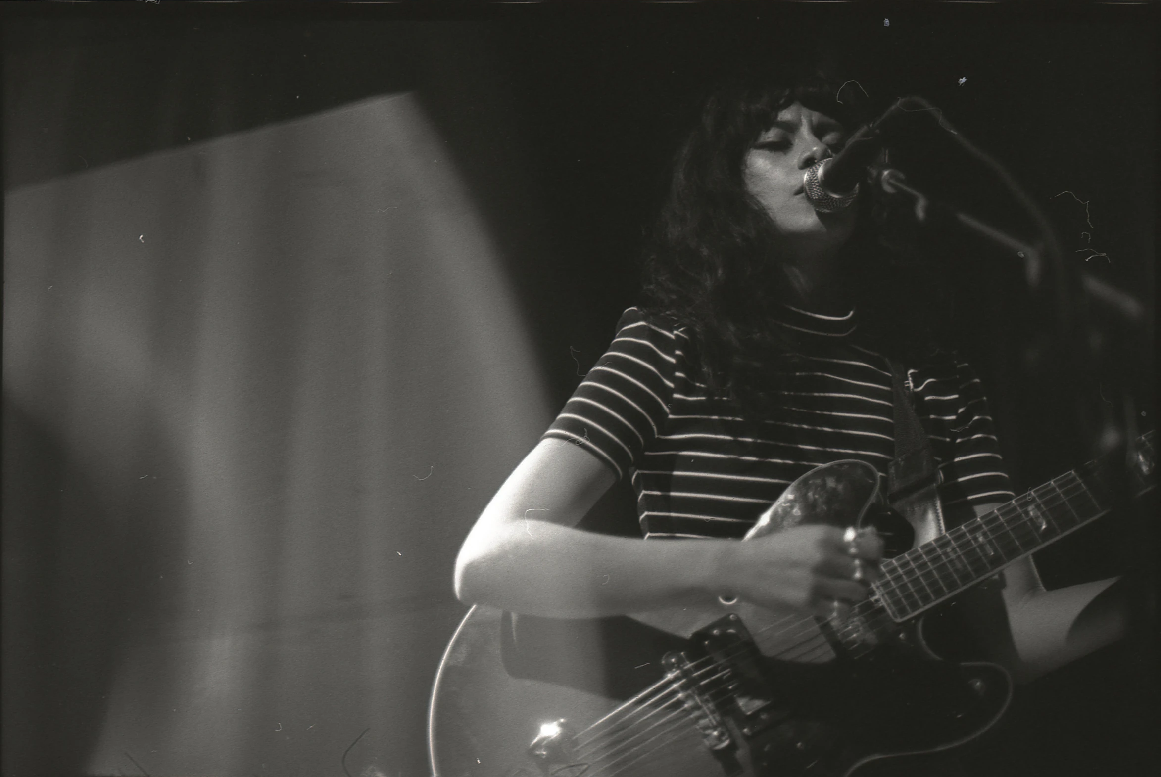 a black and white po shows an acoustic player on stage, in front of a microphone