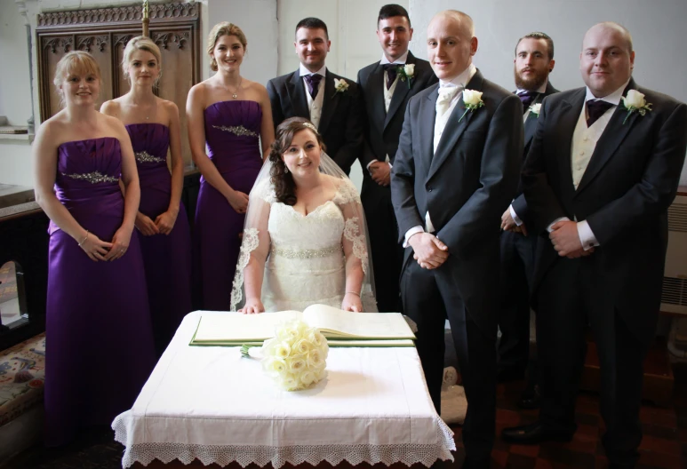 the wedding party is all standing next to the cake