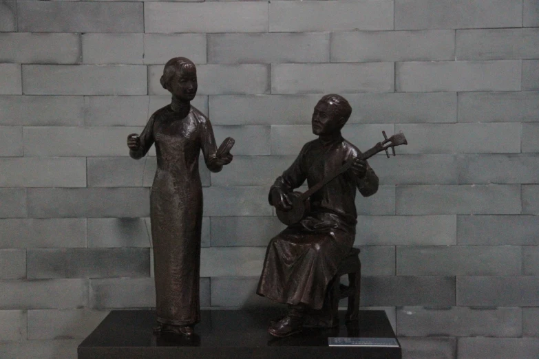 two bronze statues holding instruments near a stone wall