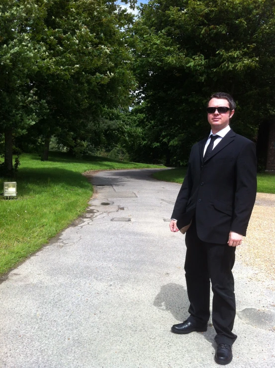 a man wearing sunglasses and a black suit is standing in the street