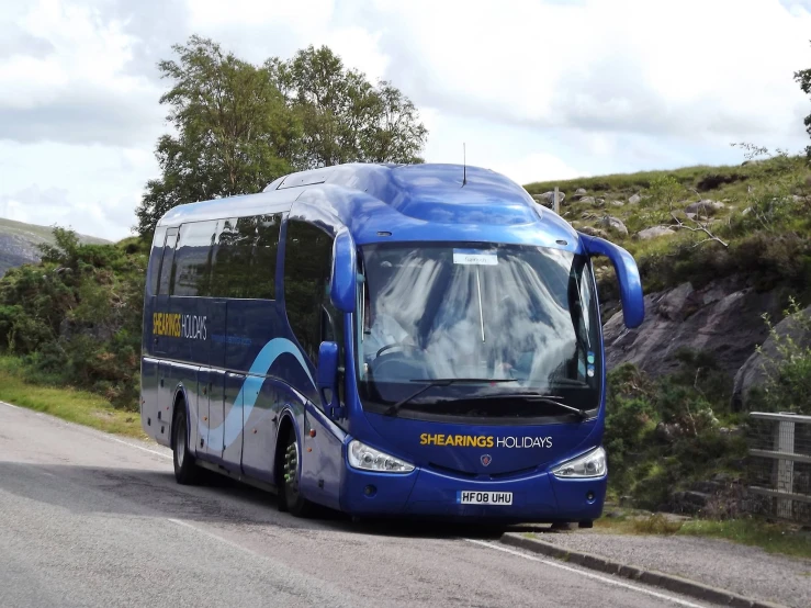 a blue bus traveling down a road next to trees