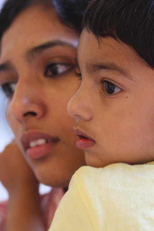 a woman and child sitting together, one with her head tilted towards the left