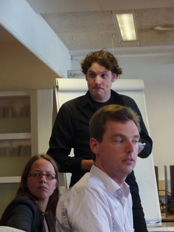 two men and a woman sitting at a desk, each holding their hands together