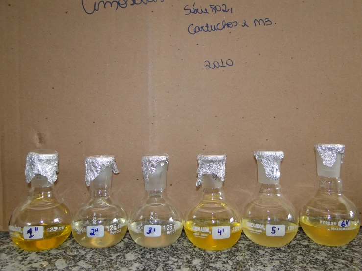 five small glass jars containing yellow liquid lined up in a row