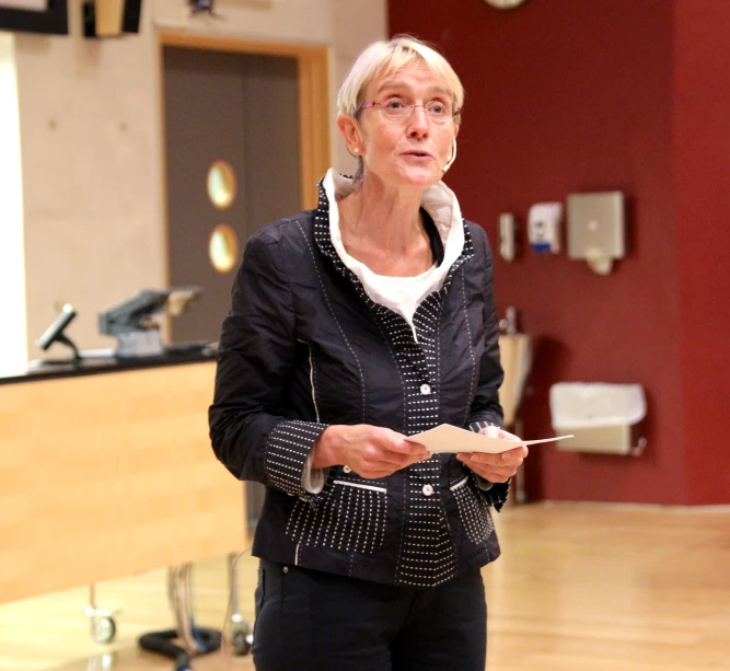 a woman standing and pointing to her paper with a black jacket