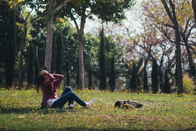 a woman sitting in the grass in front of a tree