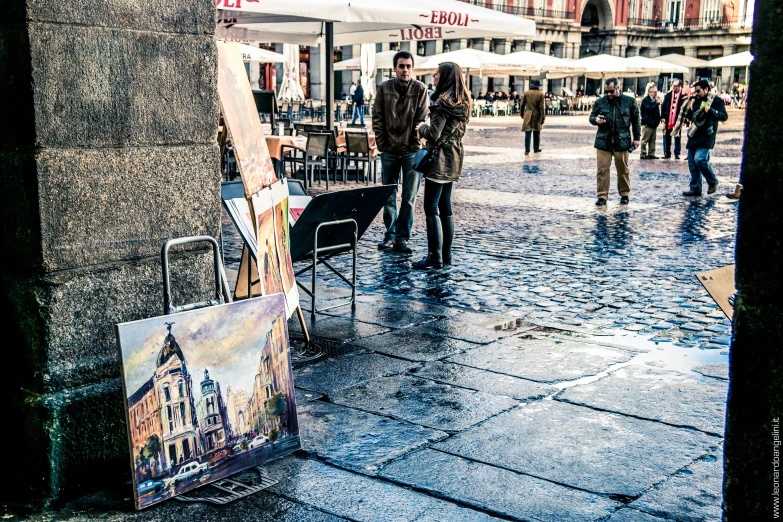 two people stand next to a street with paintings and artwork