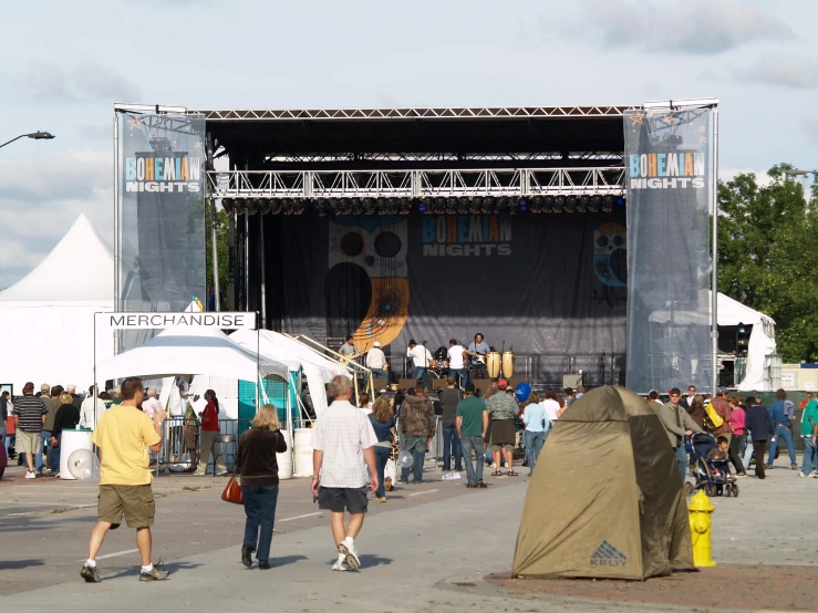 a crowd of people walking by an outdoor stage