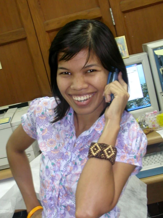 a smiling lady talks on the phone while sitting at the desk