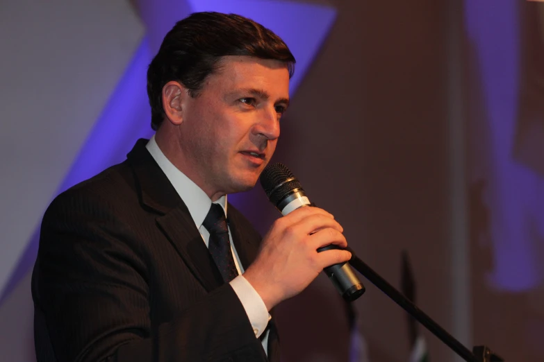 a man speaking at an event in a business suit
