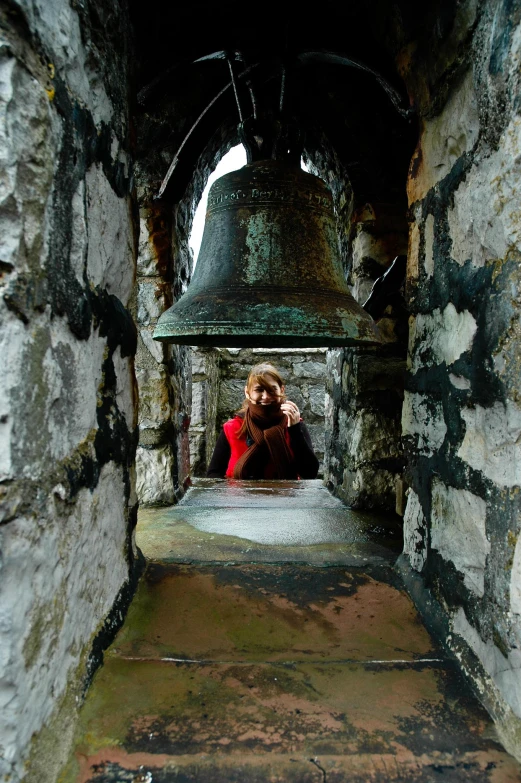 a woman sitting inside a tunnel with a big bell