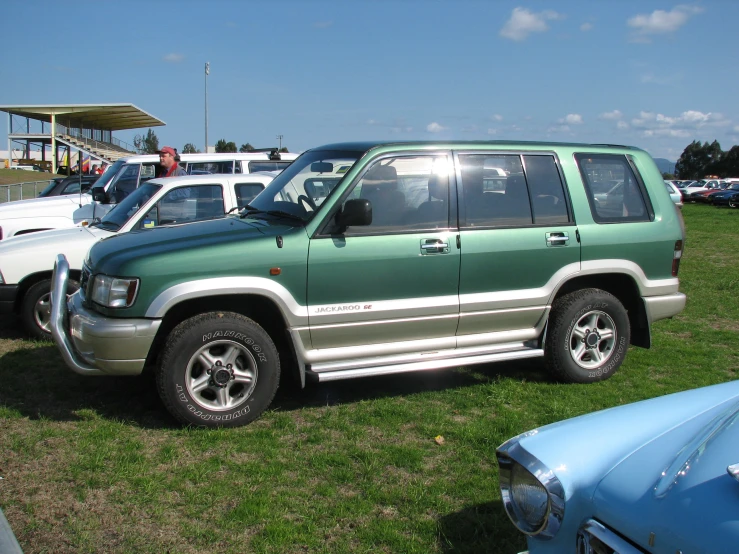 a green suv parked in the grass at a car show