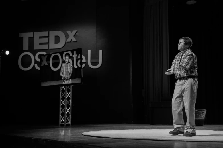 a man stands in a black and white po as he speaks on stage