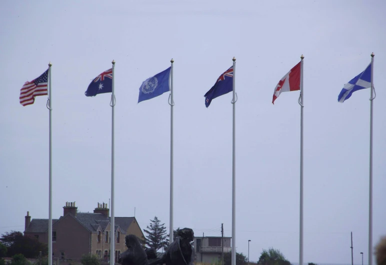 several flags of different colors, in a line, fly against a gray sky